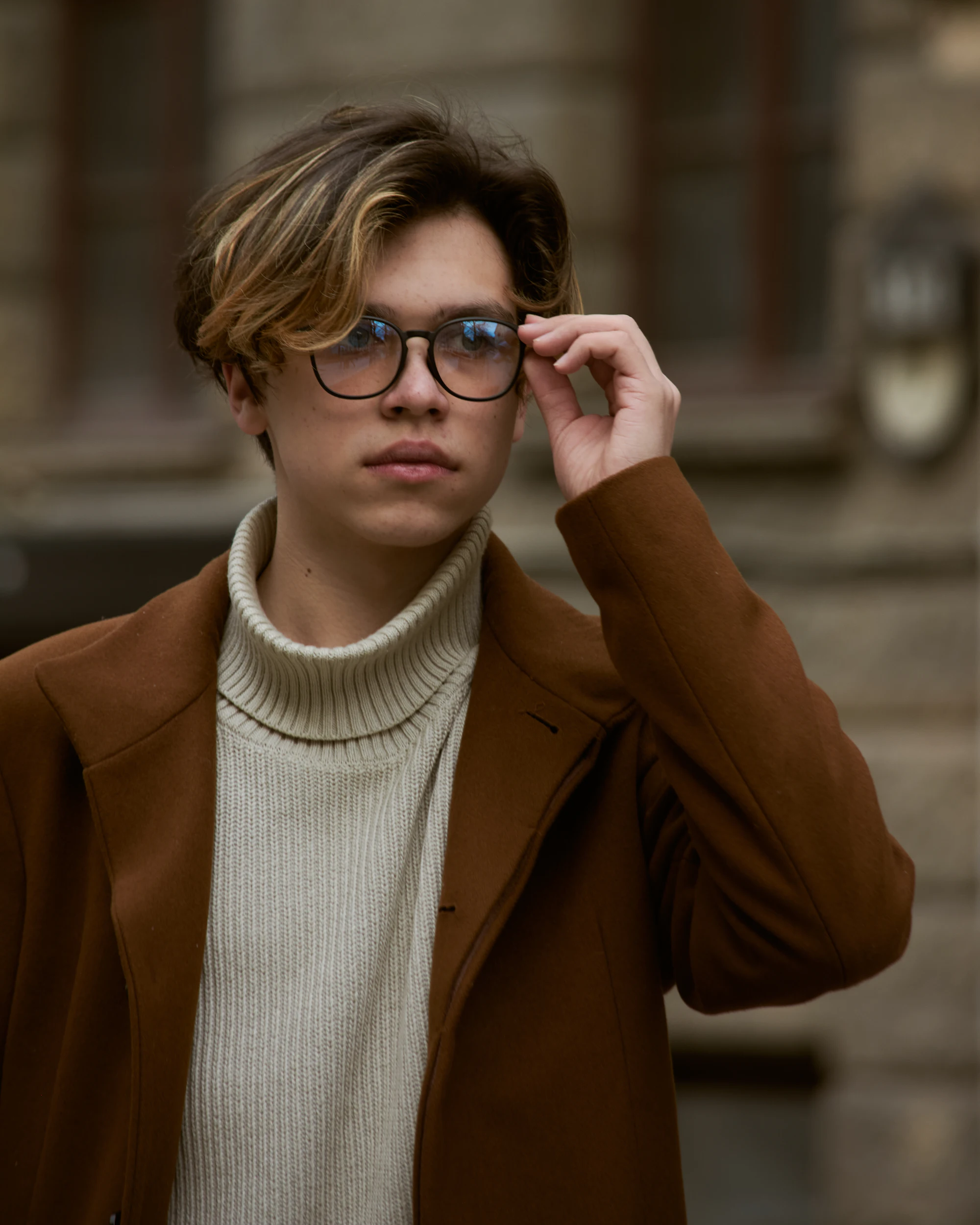 Man in a camel coat adjusting tortoiseshell eyeglasses