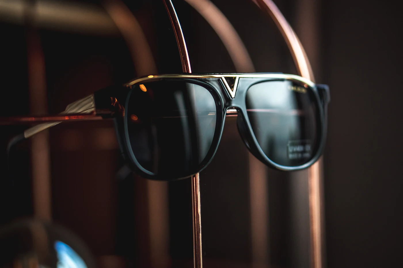 Gold-bridged aviator sunglasses displayed on a brass stand
