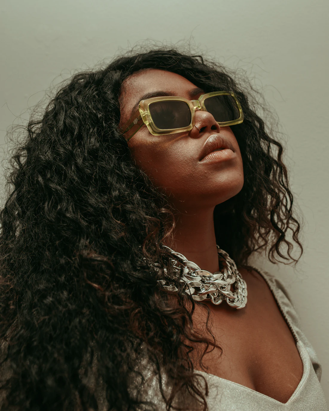 Woman with curly hair wearing gold rectangular sunglasses